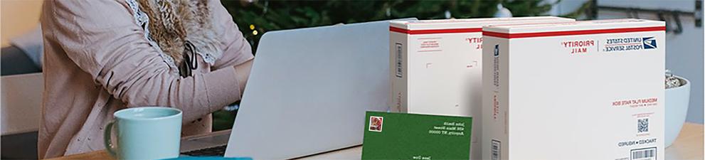 一位女士在手提电脑前准备运送优先邮箱和印有节日主题邮票的卡片.